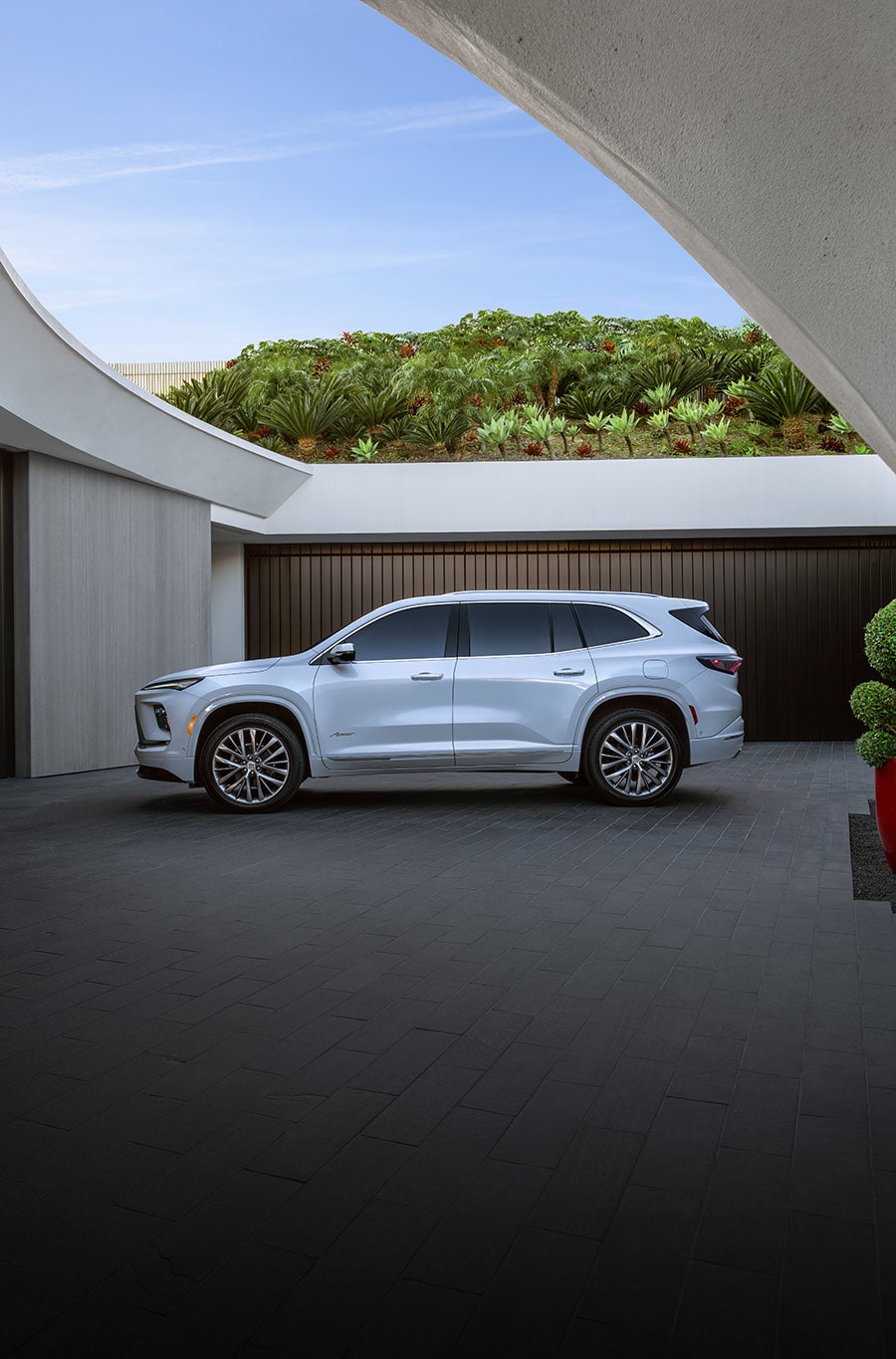 A White Buick Enclave SUV is Parked on a Road Next to a Rocky Ocean Beach Under a Clear Sky