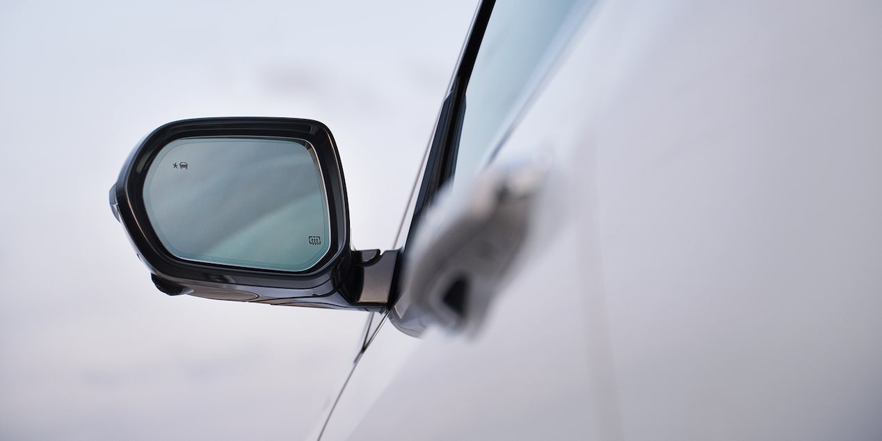 Three Quarters Rear View of a 2026 White Buick Enclave Driving Down the Road Next to Mountains and a Body of Water